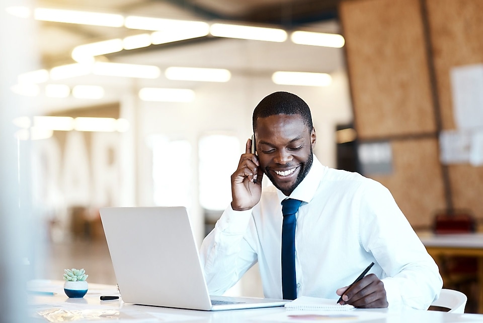 Un homme noir heureux est au telephone devant son ordinateur portable et  sourit