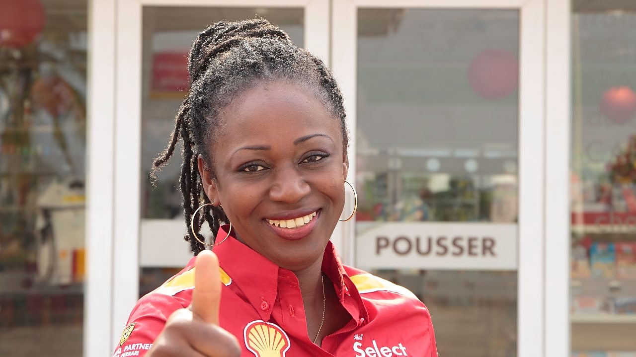 Femme souriante et accueillante devant une boutique Shell