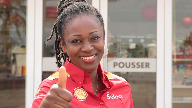 Femme souriante et accueillante devant une boutique Shell