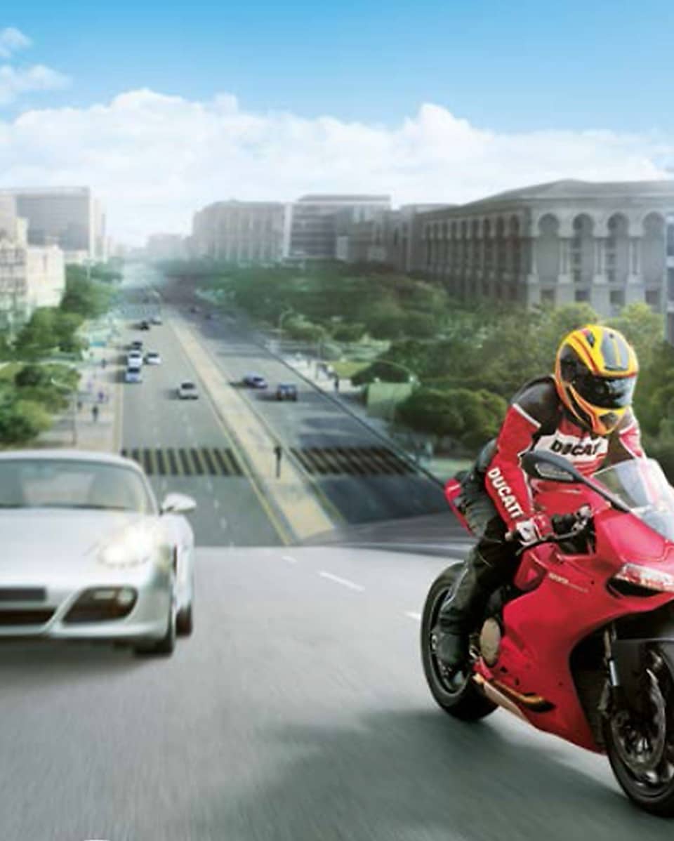 Moto rouge et conducteur casque jaune sur une route avec des voitures et des bâtiments dans l'arrière-plan.