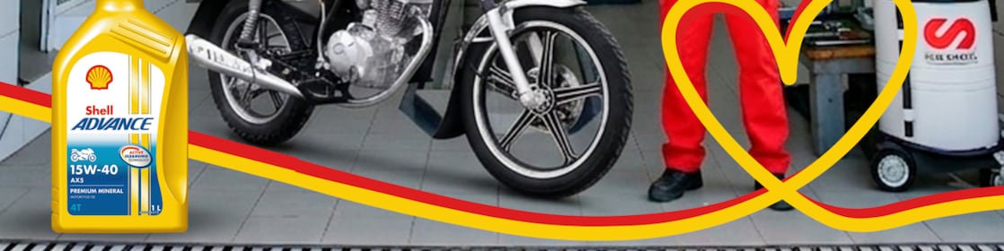 Employé en station avec une bouteille d'huile Shell Advance AX5 à côté d'une moto.