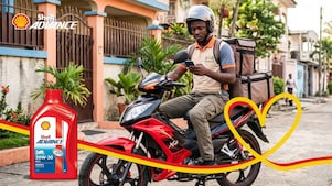 Conducteur de moto sur un scooter rouge,  téléphone à la main avec une bouteille d'huile Advance AX3 au dessus de l'image.