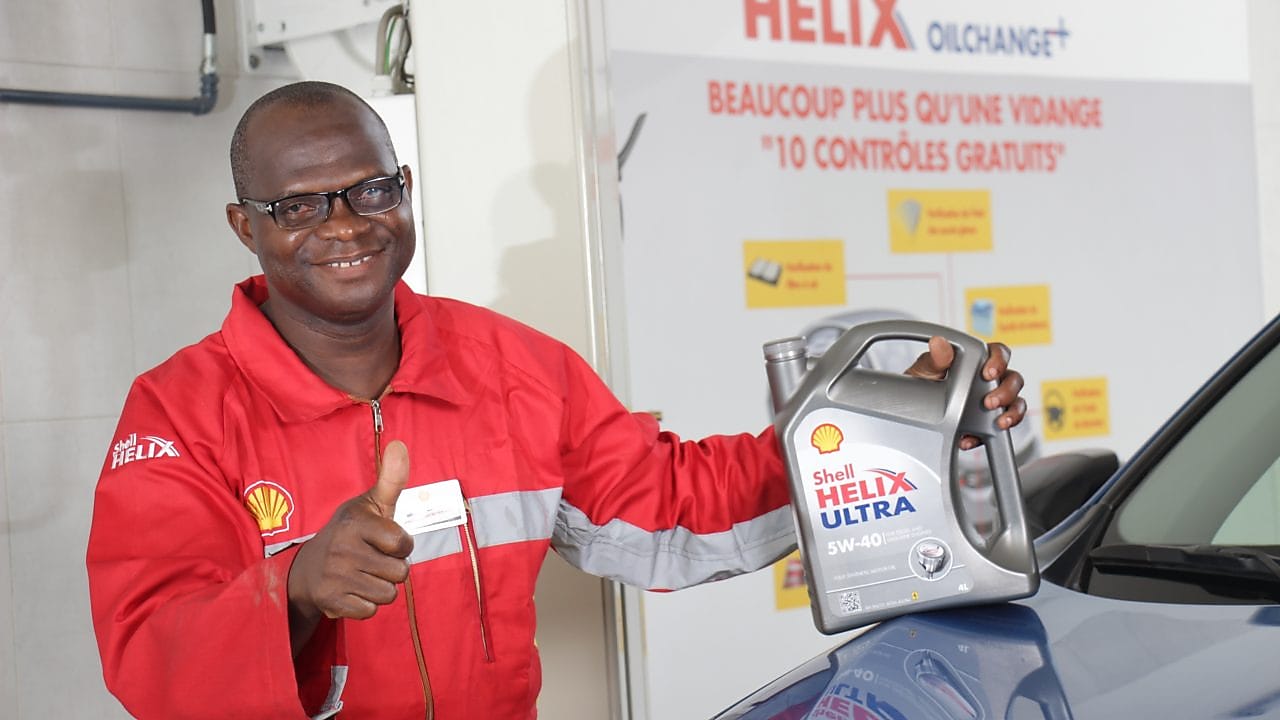 Technicien Shell tenant une bouteille d'huile Shell Helix devant un véhicule dans une station service shell.