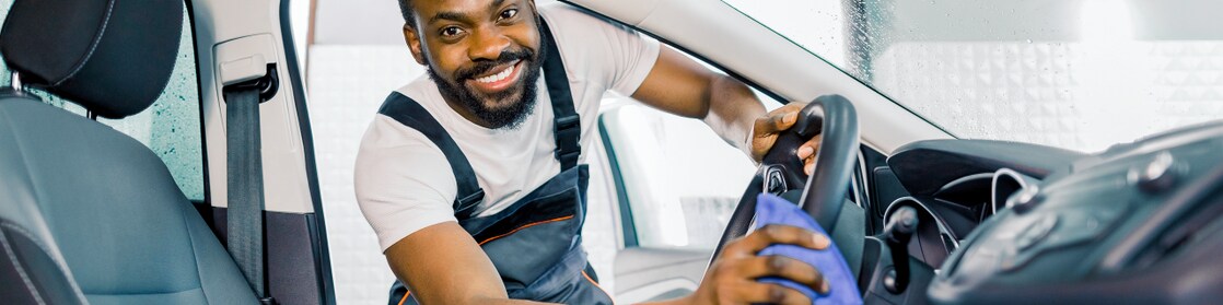 Technicien souriant nettoyant l'intérieur d'une voiture avec des produits Shell Car Care pour un habitacle propre et soigné