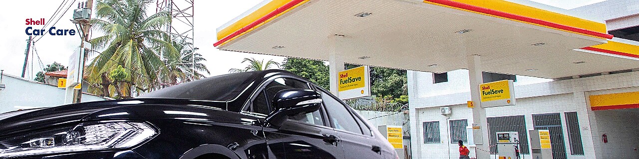 Station Shell avec un véhicule noir brillant au premier plan, illustrant l’efficacité des produits de nettoyage extérieur Shell Car Care
