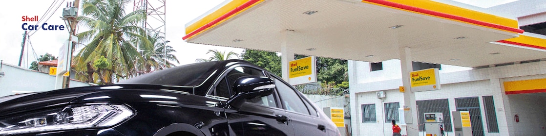 Station Shell avec un véhicule noir brillant au premier plan, illustrant l’efficacité des produits de nettoyage extérieur Shell Car Care