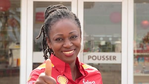 Femme souriante et accueillante devant une boutique Shell